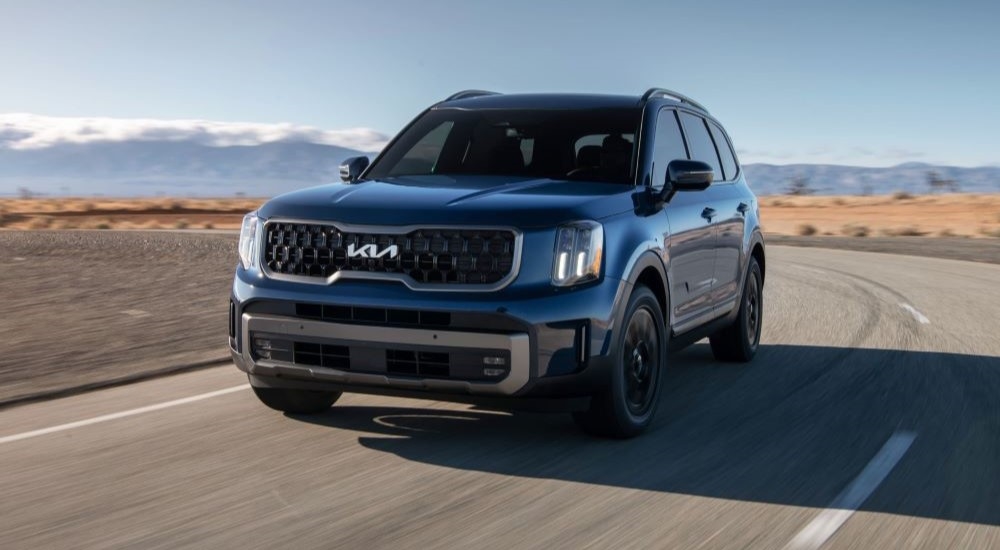 Blue 2025 Kia Telluride for sale near Jersey Village driving around a bend.
