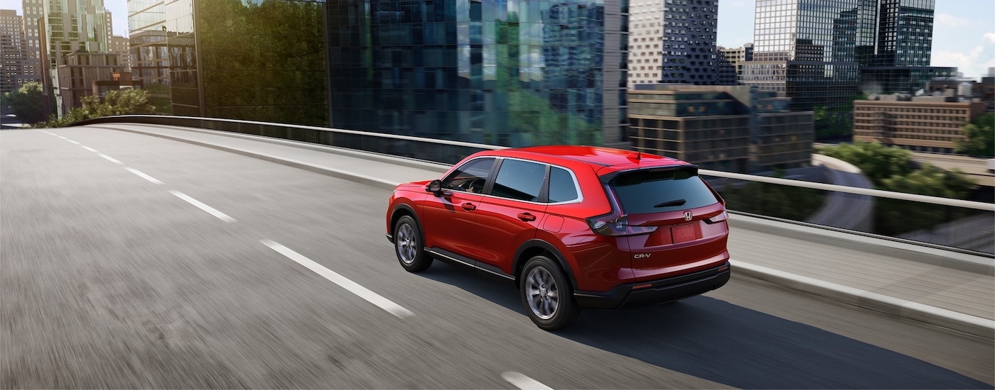 Rear of a red 2025 Honda CR-V driving across a bridge.