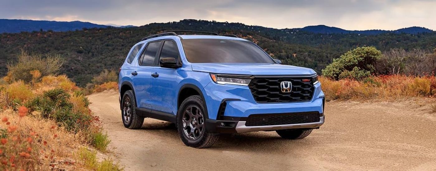 A blue 2025 Honda Pilot TrailSport off-roading on a dirt road