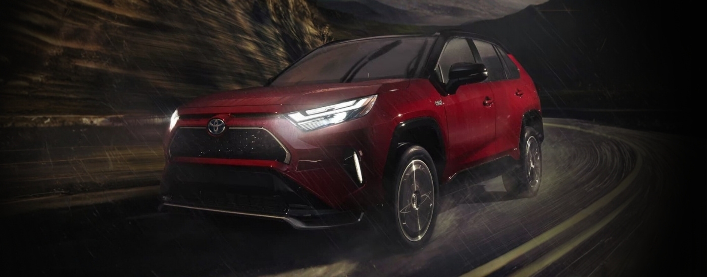 Red 2023 Toyota RAV4 PHEV driving on a rainy night
