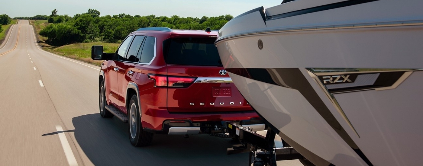 Red 2023 Toyota Sequoia towing a boat on a highway
