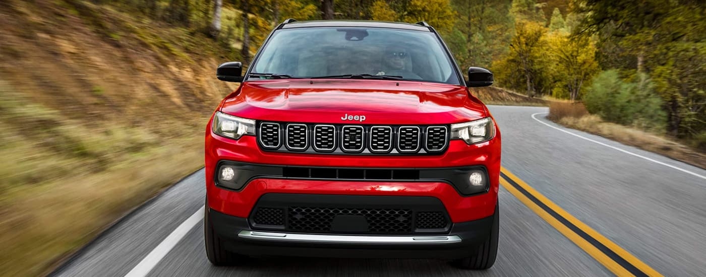 Front of a red 2025 Jeep Compass driving down an open road.