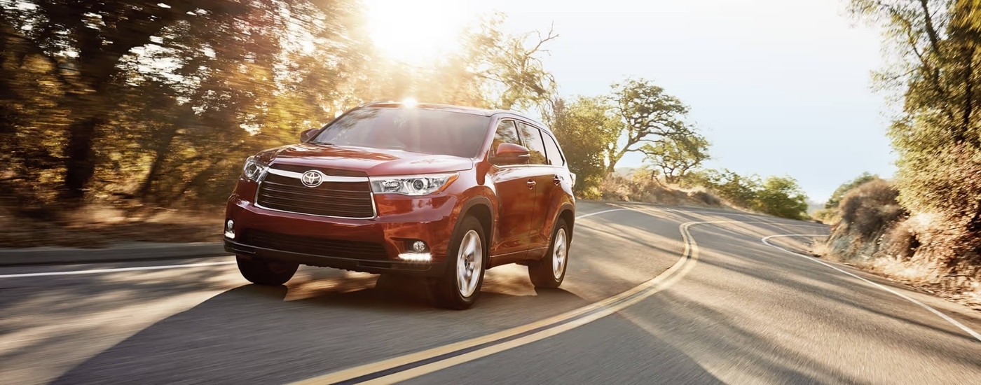 Red 2016 Toyota Highlander driving to look at a used Toyota for sale in Westminster