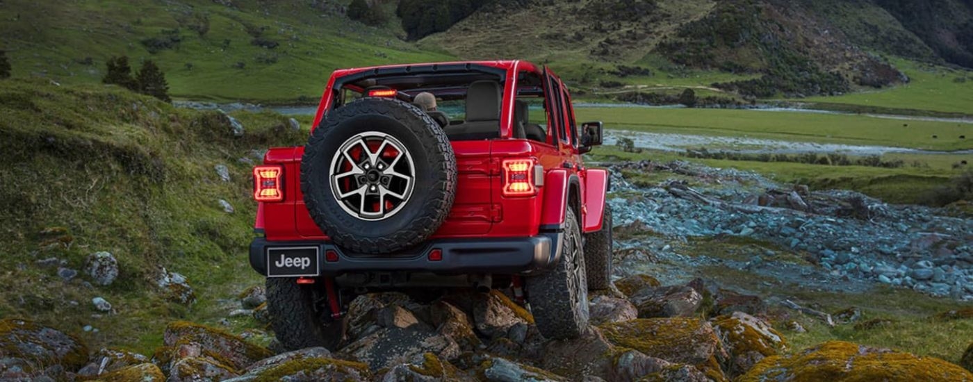Rear of a red 2025 Jeep Wrangler driving off-road.