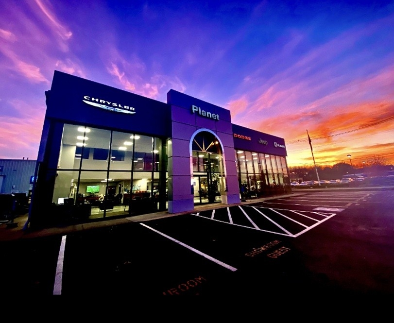 A picture of the showroom of Planet Chrysler Jeep Dodge Ram with the sun setting behind it.