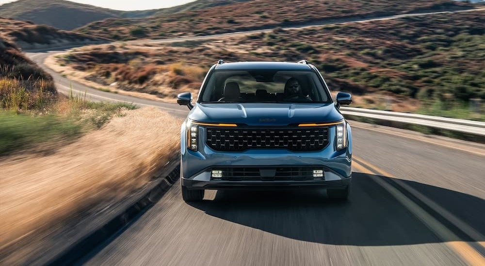 A blue 2026 Kia Carnival driving on a highway.