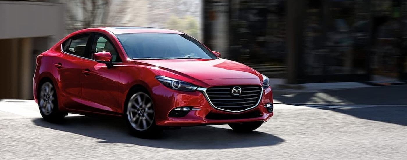 A red 2018 Mazda3 driving in a city.