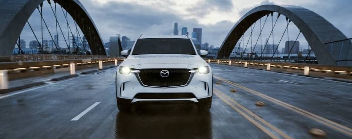 A white 2024 Mazda CX-90 driving on a bridge.