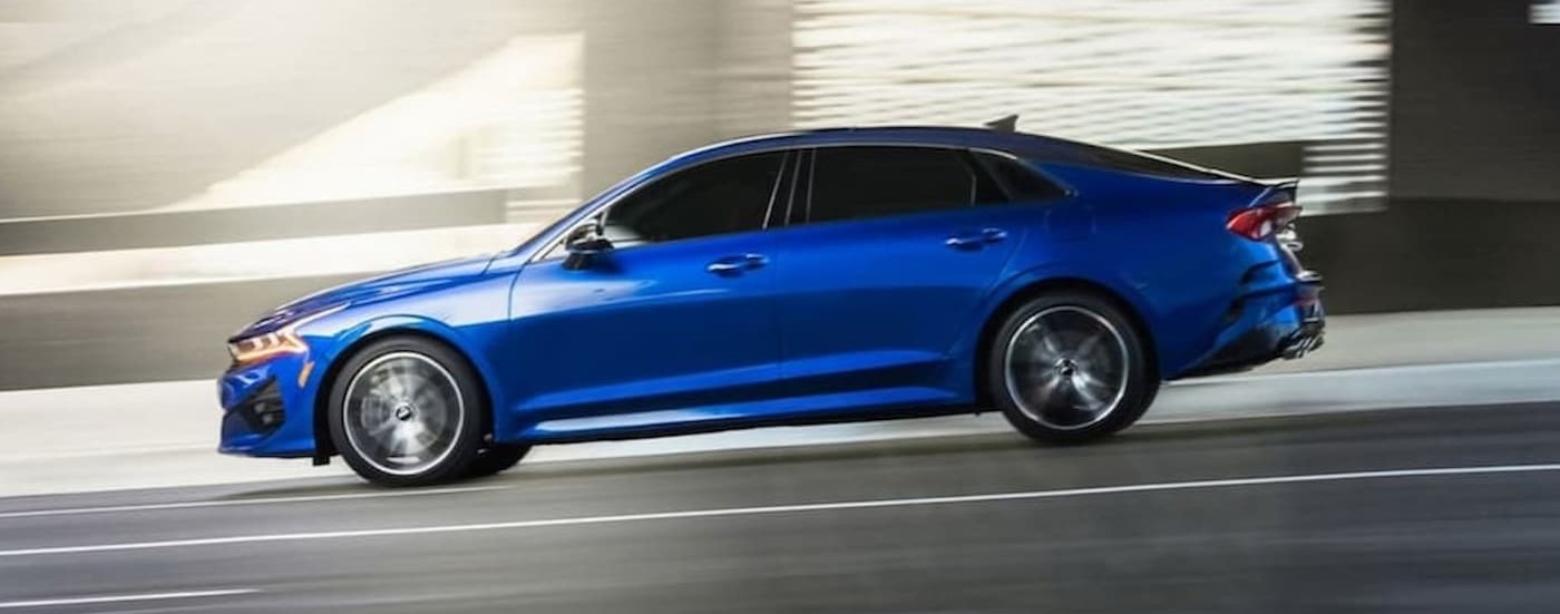 A blue 2024 Kia K5 GT driving on a highway.