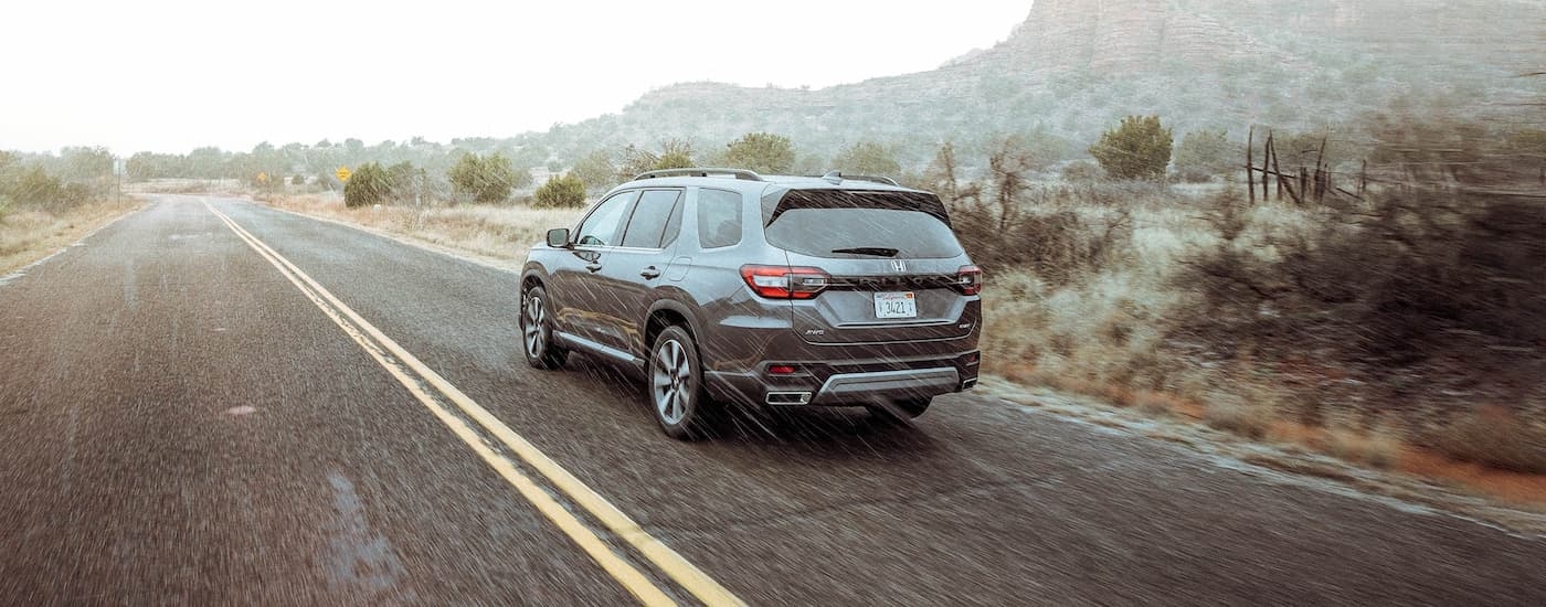 Rear of a grey 2025 Honda Pilot driving down an open road.