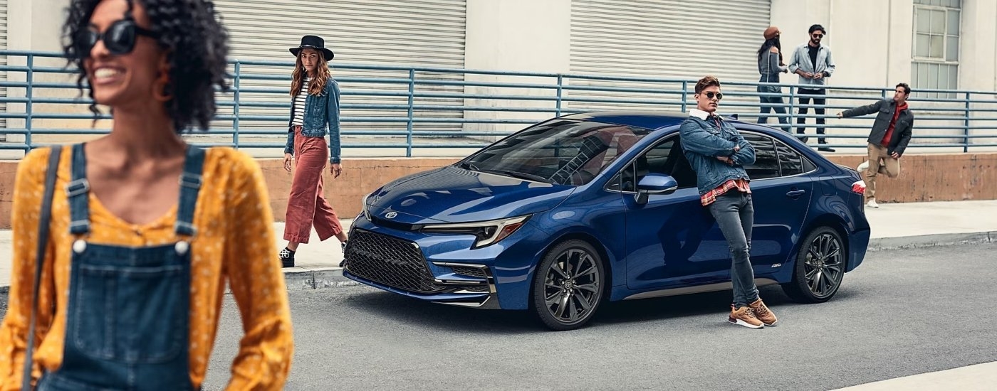 People posing near a blue 2026 Toyota Corolla for sale near Bennington parked by a sidewalk.