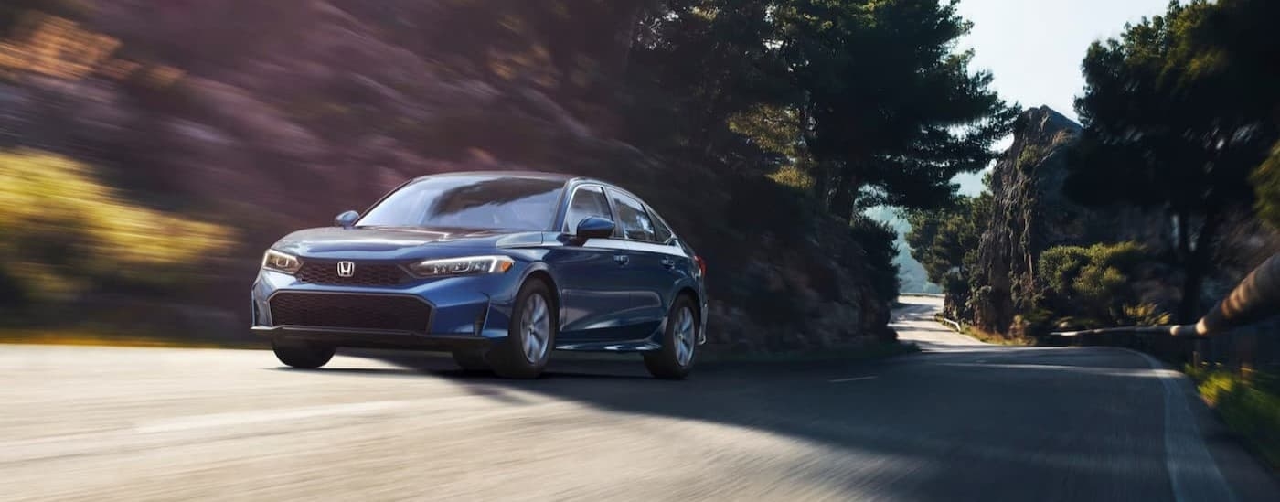 A blue 2025 Honda Civic for sale in Hillside driving on a highway.