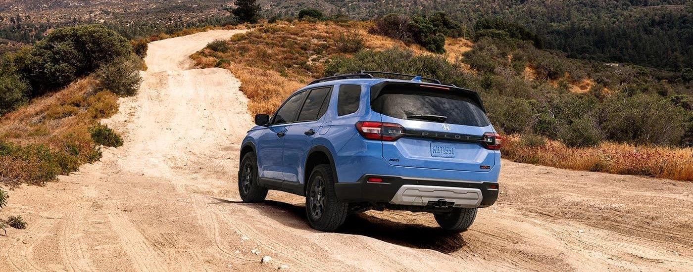 Rear of a blue 2025 Honda Pilot driving off-road.