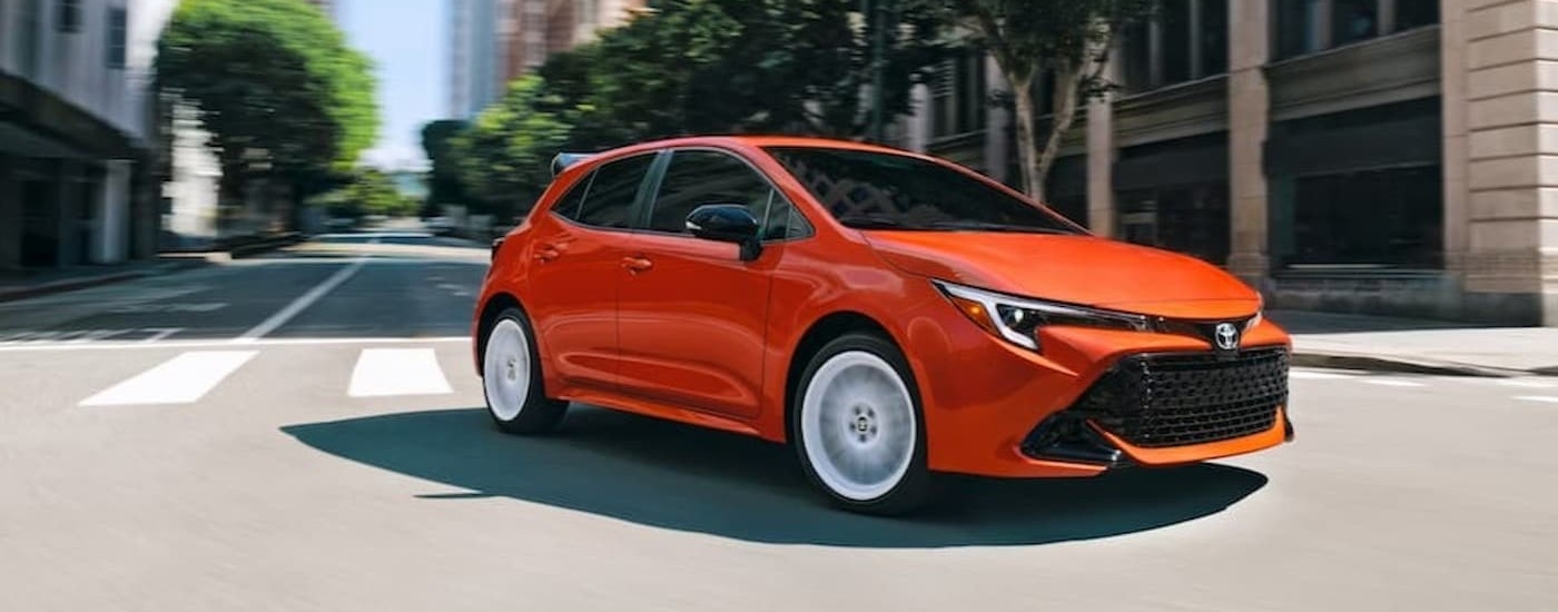 An orange 2026 Toyota Corolla Hatchback driving in a city.