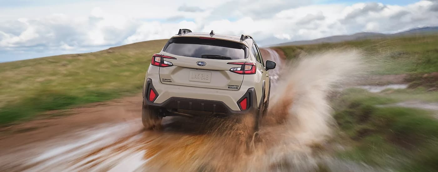 Rear of a white 2026 Subaru Crosstrek Hybrid driving on a muddy road