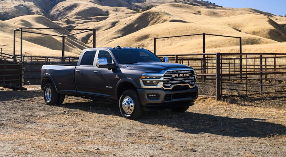 Black 2026 Ram 3500 driving off-road near a fence.