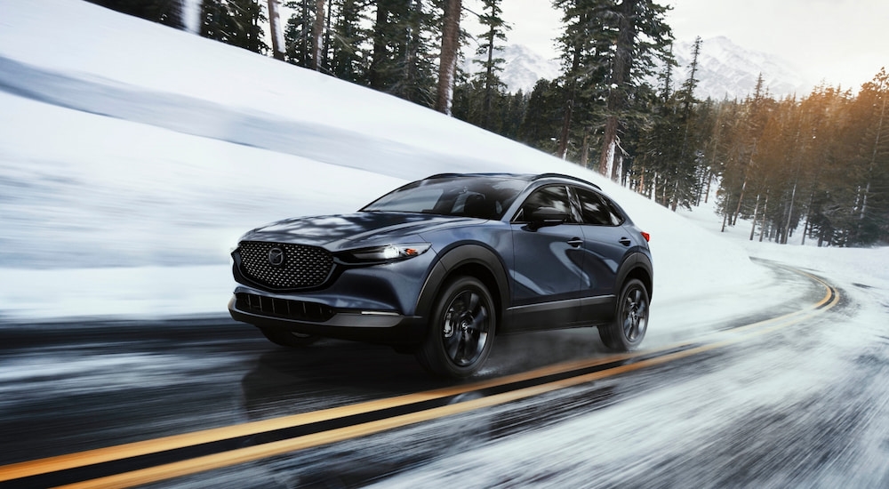 Grey 2026 Mazda CX-30 for sale driving around a bend on a snowy road.