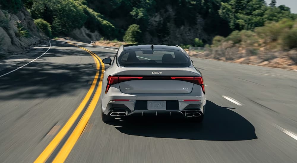 Grey rear of a 2026 Kia K5 driving on a winding road