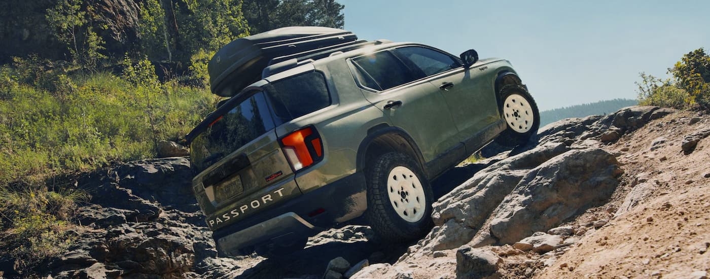 A green 2025 Honda Passport TrailSport Elite off-roading on rocks