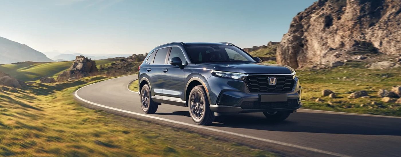 Blue 2025 Honda CR-V Hybrid for sale near Bellevue driving around a bend.