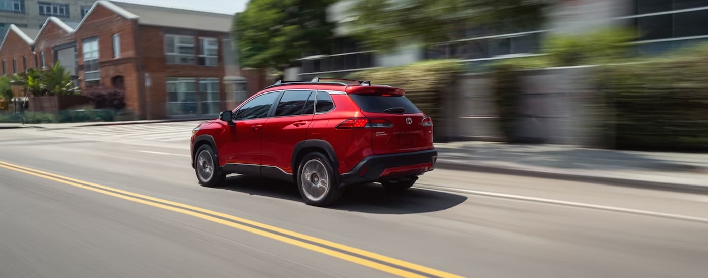 Rear of a red 2025 Toyota Corolla Cross driving down a road.