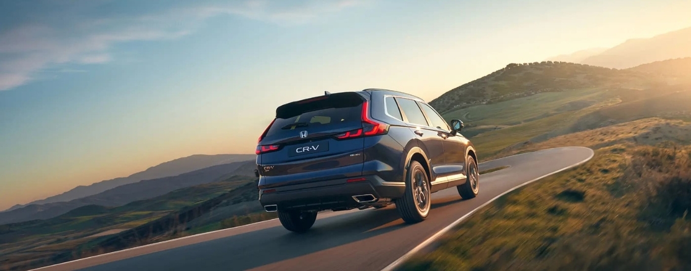 Rear of a blue 2025 Honda CR-V Hybrid driving on a winding road.