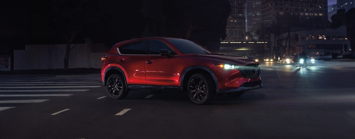 Red 2025 Mazda CX-5 for sale near Tomball driving through an intersection.