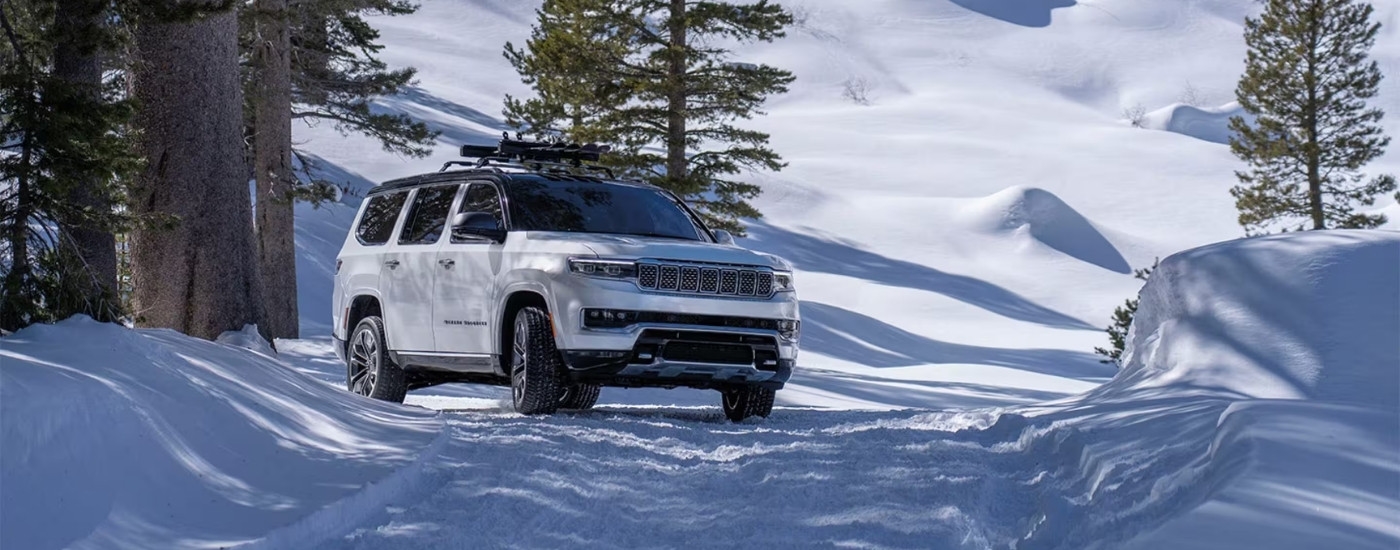White 2025 Jeep Grand Wagoneer driving on a snowy trail