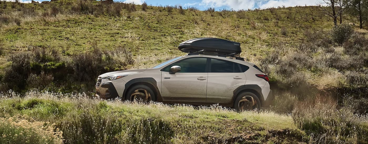 Side of a tan 2026 Subaru Crosstrek Hybrid for sale in Rhinebeck driving up a dirt road.