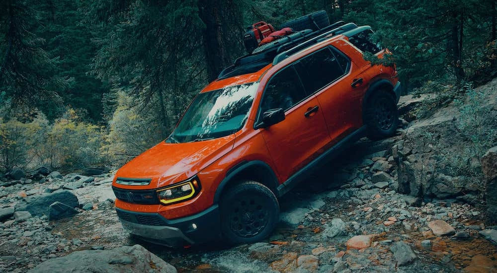 An orange 2026 Honda Passport driving off-road down a rocky hill.