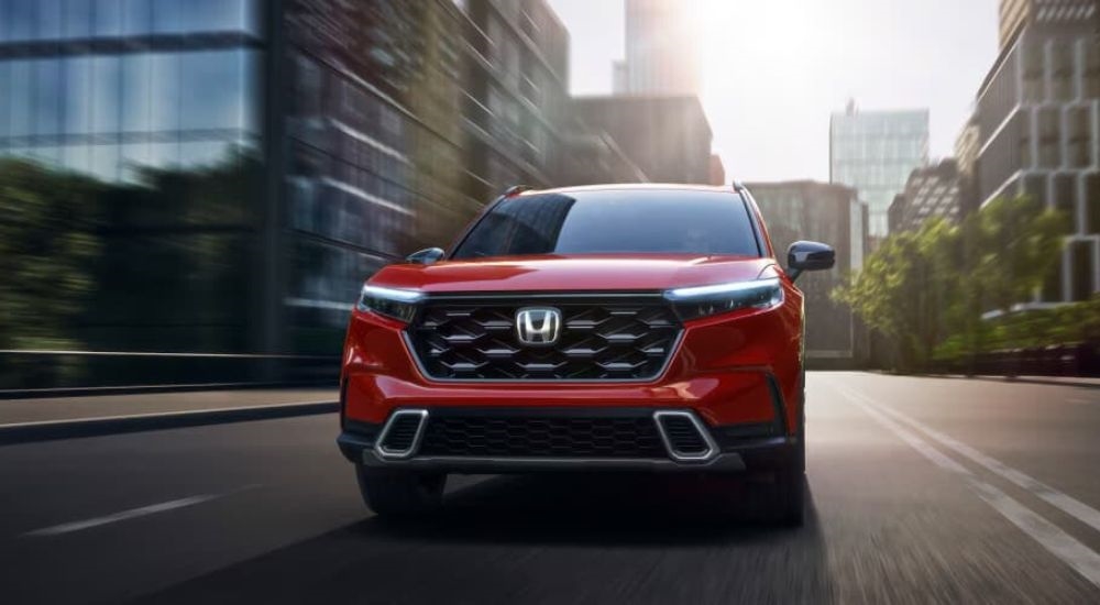 Front of a red 2025 Honda CR-V Hybrid for sale near Bellevue driving down a city street.