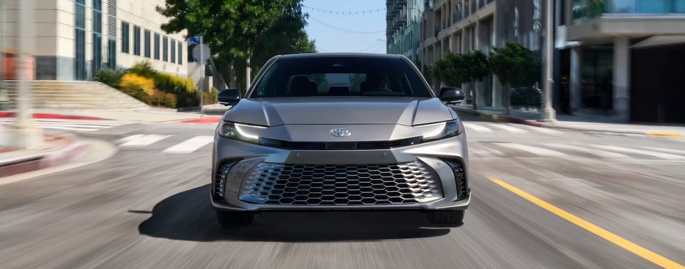 Front of a grey 2025 Toyota Camry Hybrid driving on a city street