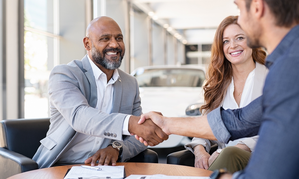 Happy car buyers shaking hands with salesperson