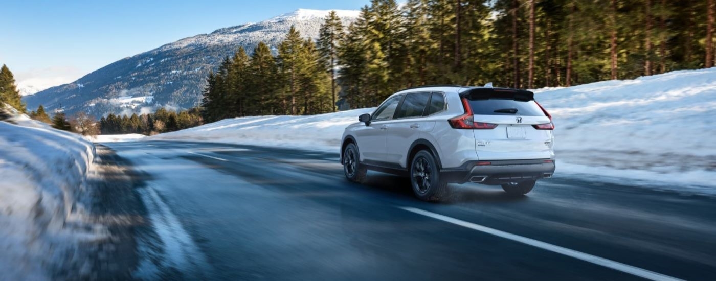 White 2023 Honda CR-V driving toward snowy mountains