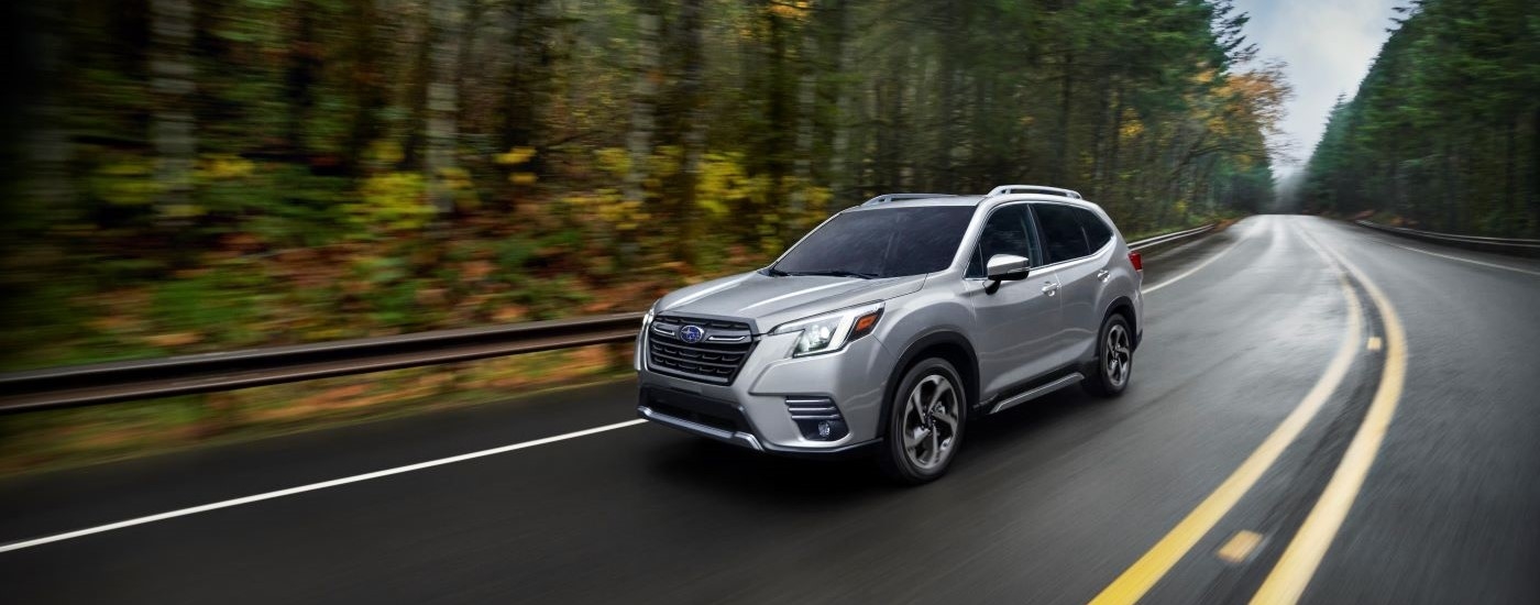 Silver 2023 Subaru Forester driving on a winding road to a used car dealership