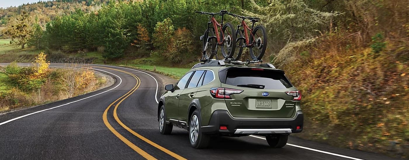 Green 2024 Subaru Outback driving on a winding road