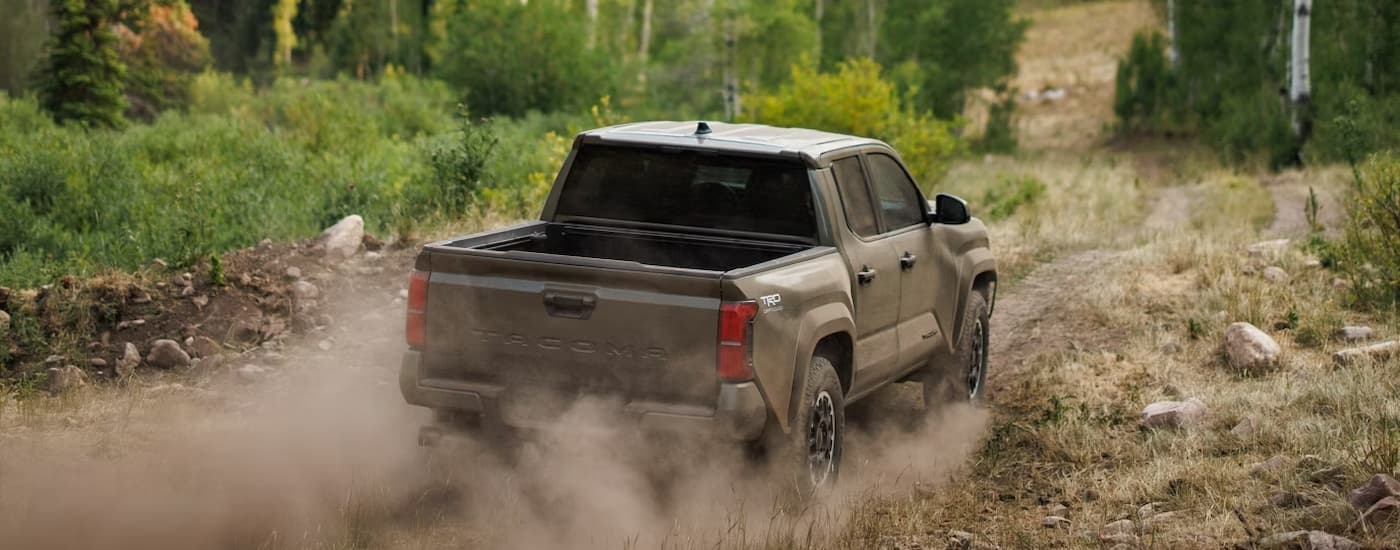 Brown 2026 Toyota Tacoma off-roading on a dirt path in the woods