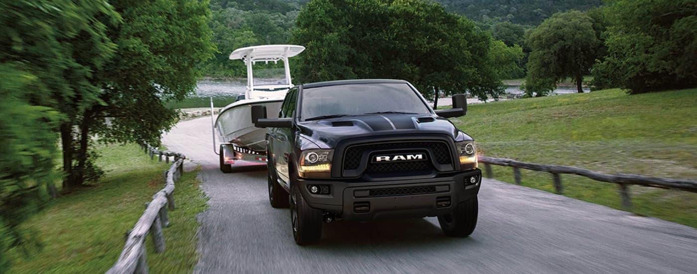 Black 2019 Ram 1500 Classic towing a boat from a used car dealership.