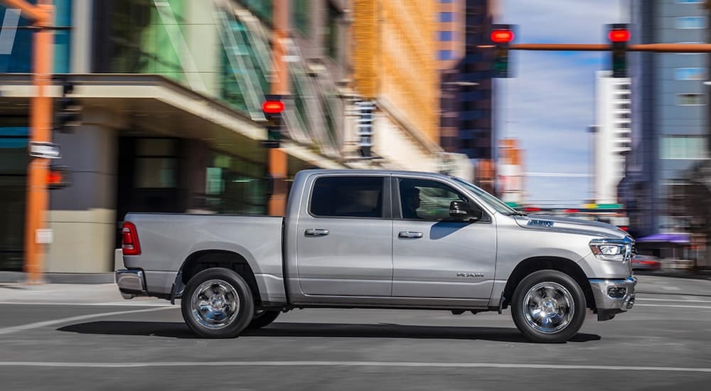 Side of a silver 2019 Ram 1500 driving down a road from a used car dealership.