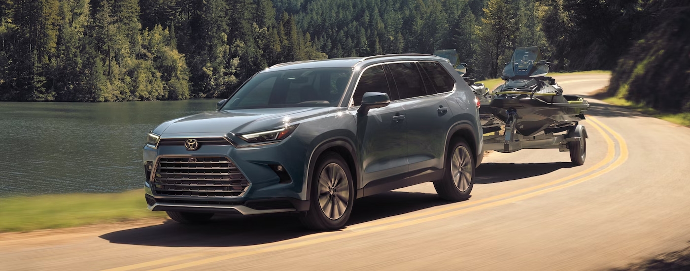 Grey 2026 Toyota Grand Highlander towing jetskis around a bend.