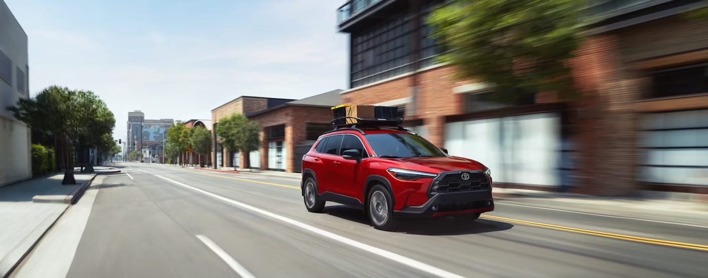 Red 2026 Toyota Corolla Cross driving down a road.
