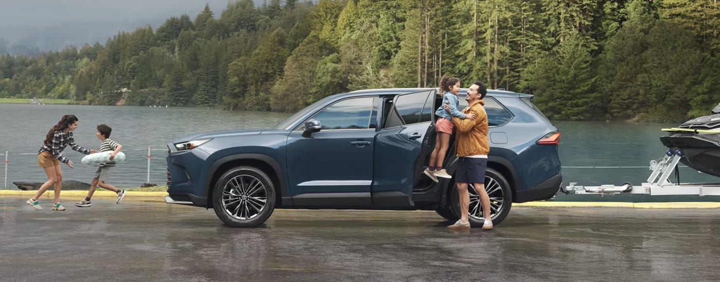 Side of a dark blue 2025 Toyota Grand Highlander for sale near New Rochelle parked near a lake.