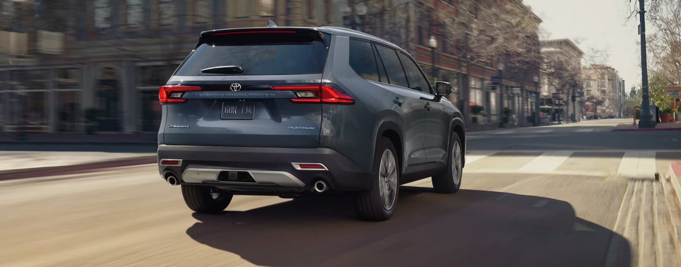 Rear of a dark blue 2026 Toyota Grand Highlander driving down a road.