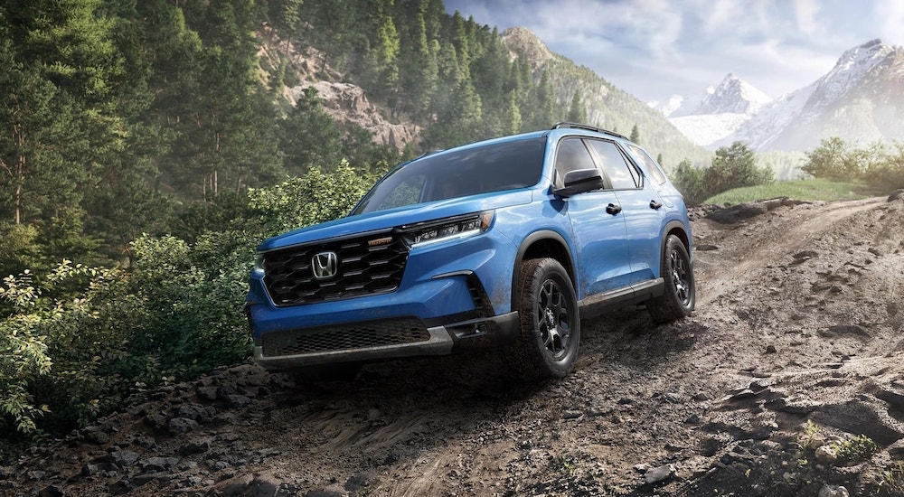 Blue 2025 Honda Pilot for sale driving down a hill.