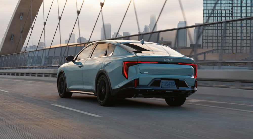 Rear of a dark green 2025 Kia K4 driving across a bridge.