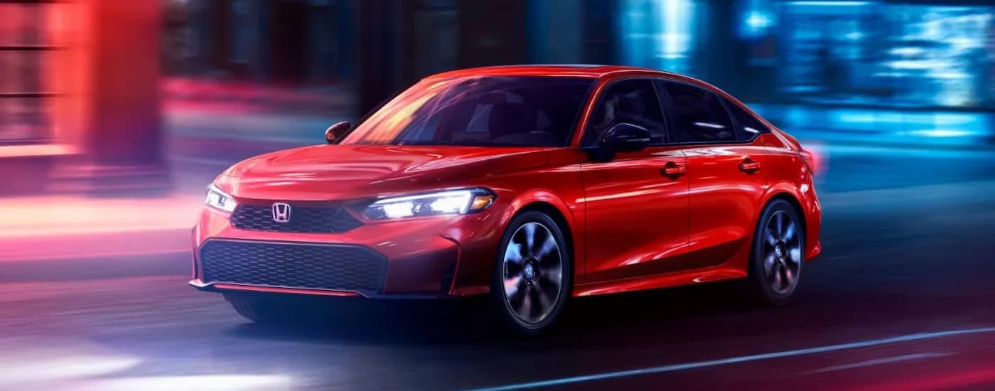 A red 2025 Honda Civic driving in a city at night