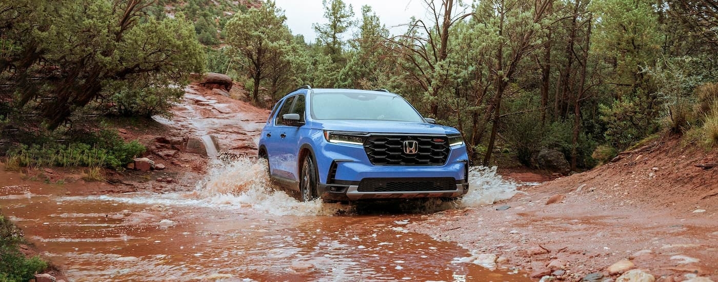 Blue 2025 Honda Pilot for sale near Arlington driving over a shallow river.