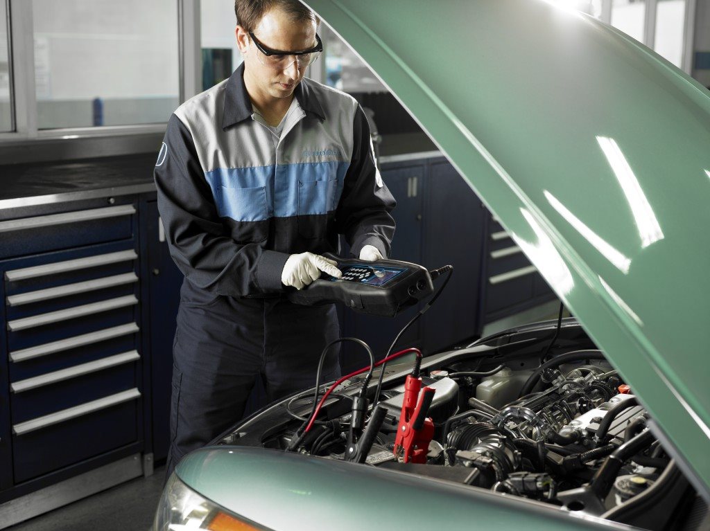 Technician testing a vehicle under the hood with a diagnostic tester