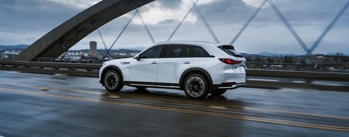 Rear of a white 2027 Mazda CX-90 Hybrid driving across a bridge.