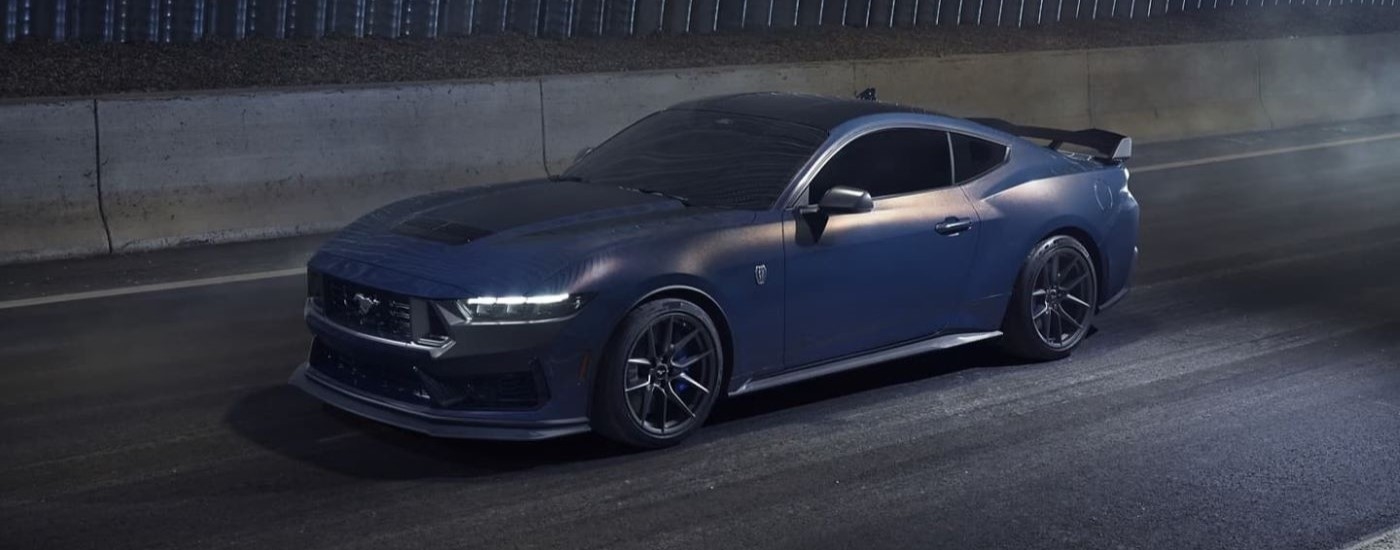 Blue 2024 Ford Mustang Dark Horse driving to a car dealership